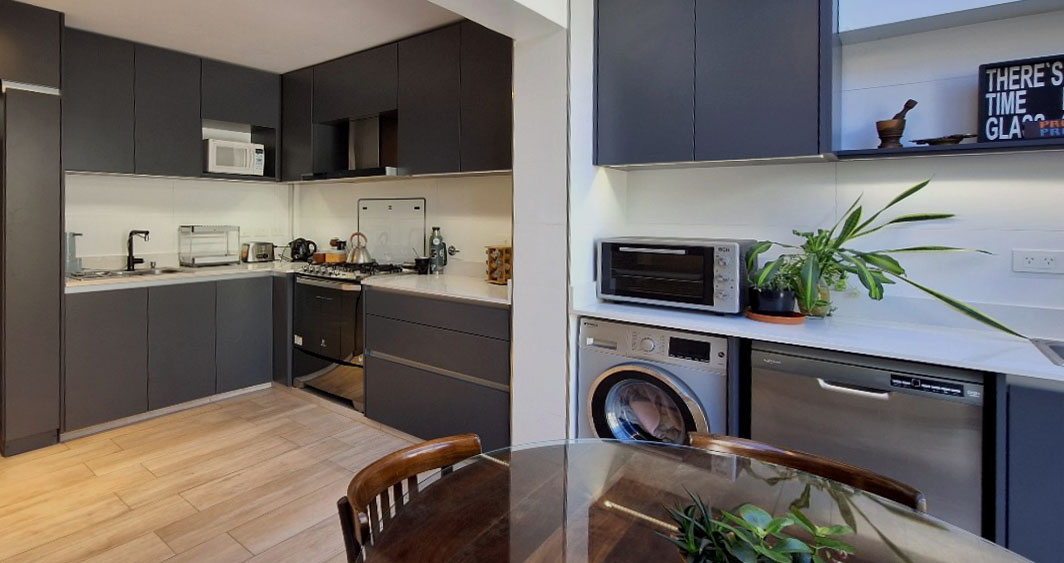 Cocina integrada con muebles oscuros, cocina a gas y lavadero